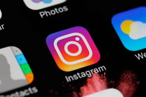 The Instagram app icon on a phone home screen, between Photos and Weather