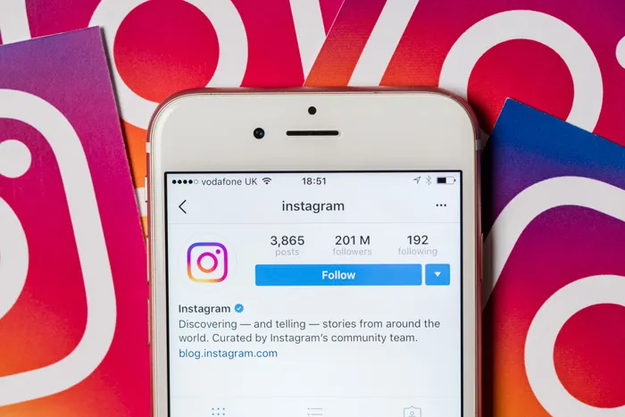 A phone showing the official Instagram account, resting on printed Instagram logos
