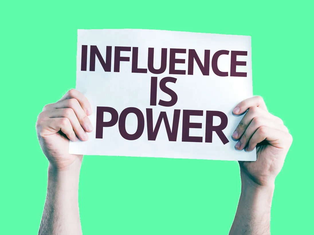Hands holding up a placard reading "INFLUENCE IS POWER" against a green background