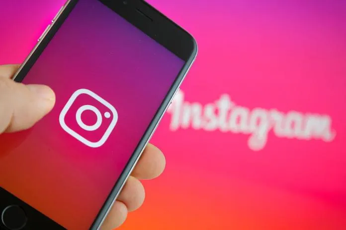 A hand holding a phone with the Instagram logo against a pink and orange background