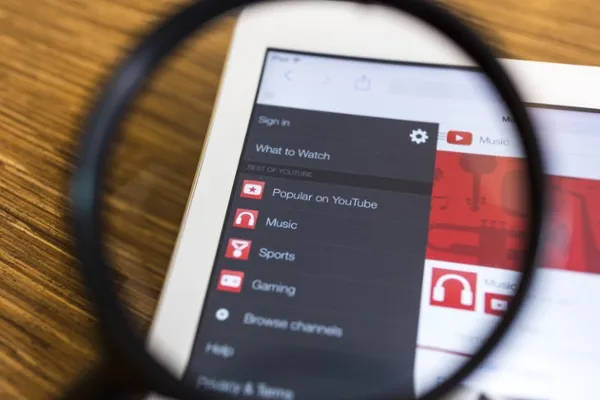 A magnifying glass over a tablet showing the YouTube browse menu
